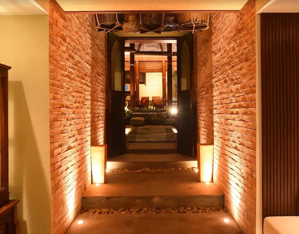 A brick passage with lamps and pebbles leading to an open door at V-Senses Wellness & Spa