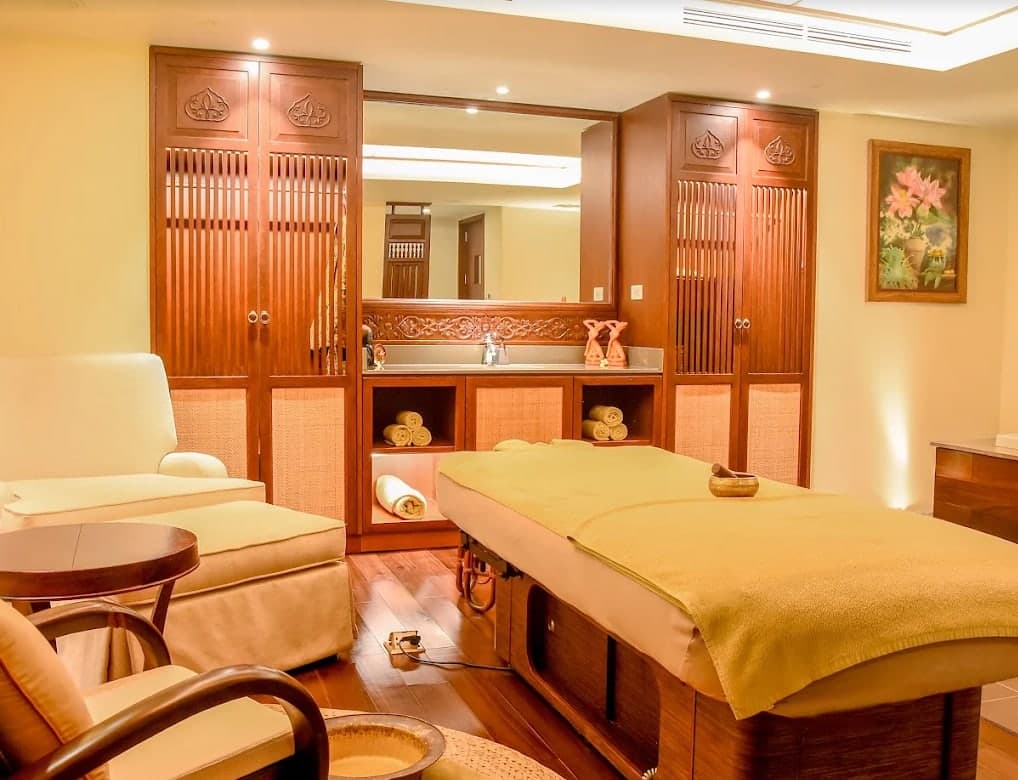 A bright treatment room at V-Senses Wellness & Spa: a bed, a mirror and carved wooden cabinets