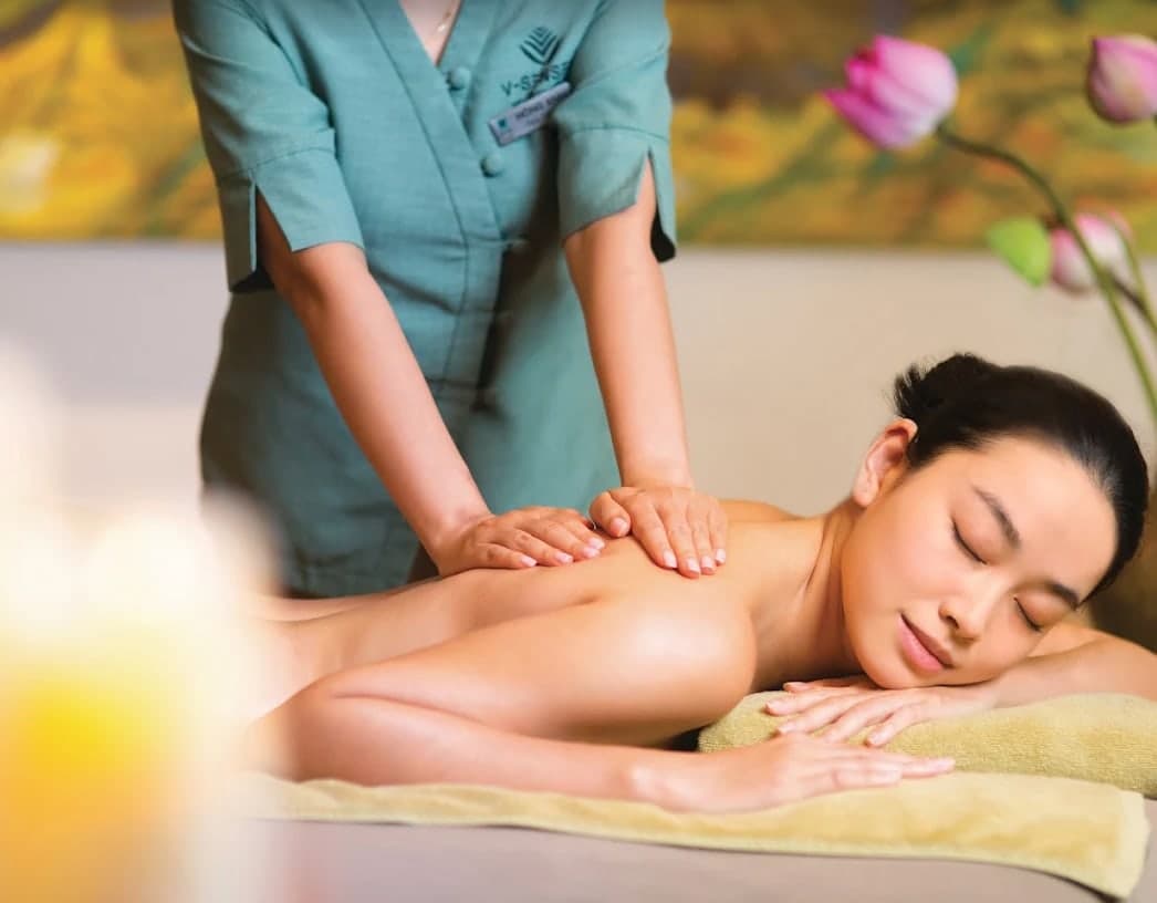 A therapist at V-Senses Wellness & Spa massages a woman's back, with lotus flowers behind