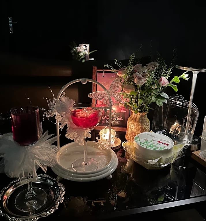 A table set for a celebration at Vấn Cocktail Bar, with flowers, a small cake and a red cocktail