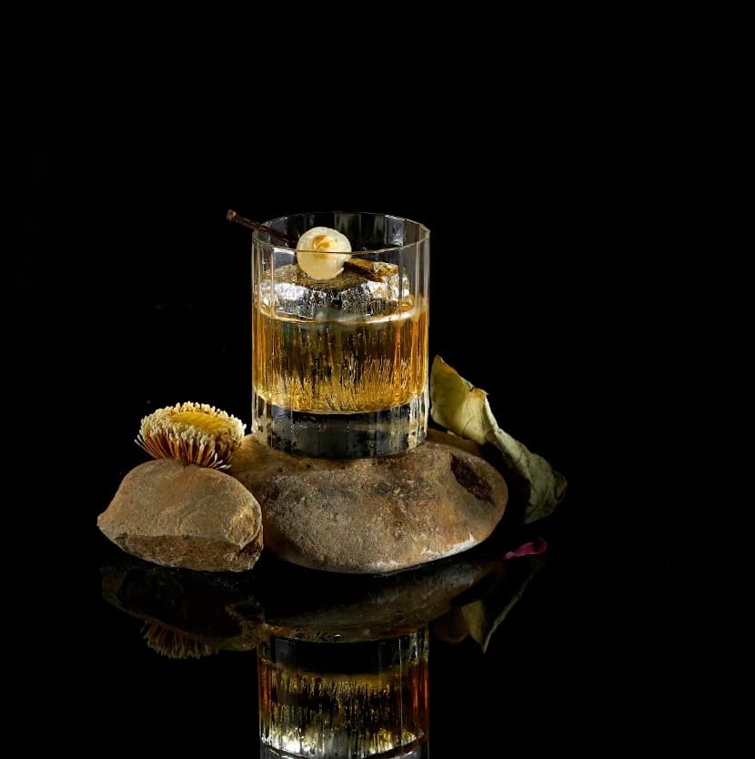 A cocktail served on a river stone with a dried flower beside it at Vấn Cocktail Bar